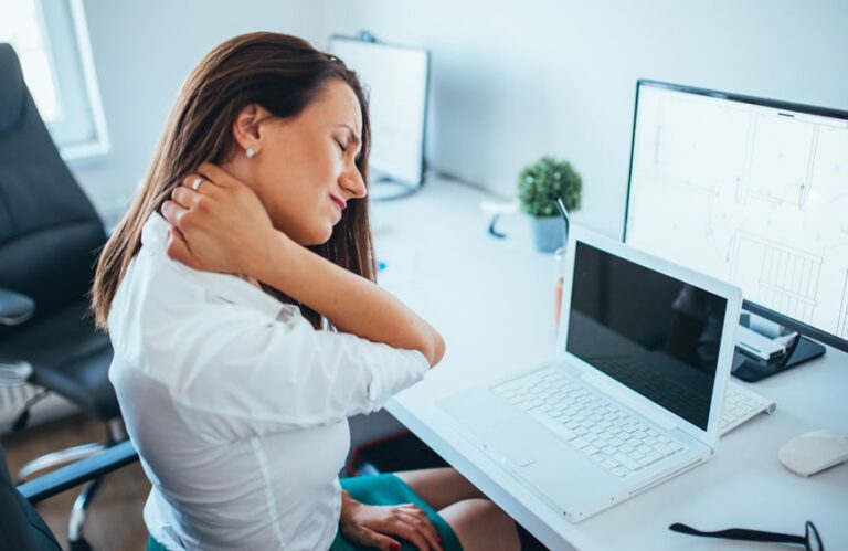 Woman gripping her neck in pain in front of a computer