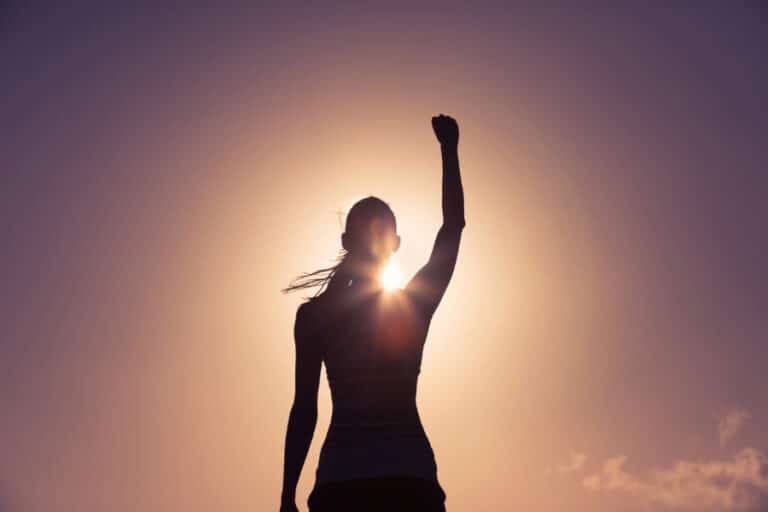 Silhouette of a woman pumping her fist in the air with the sun behind her