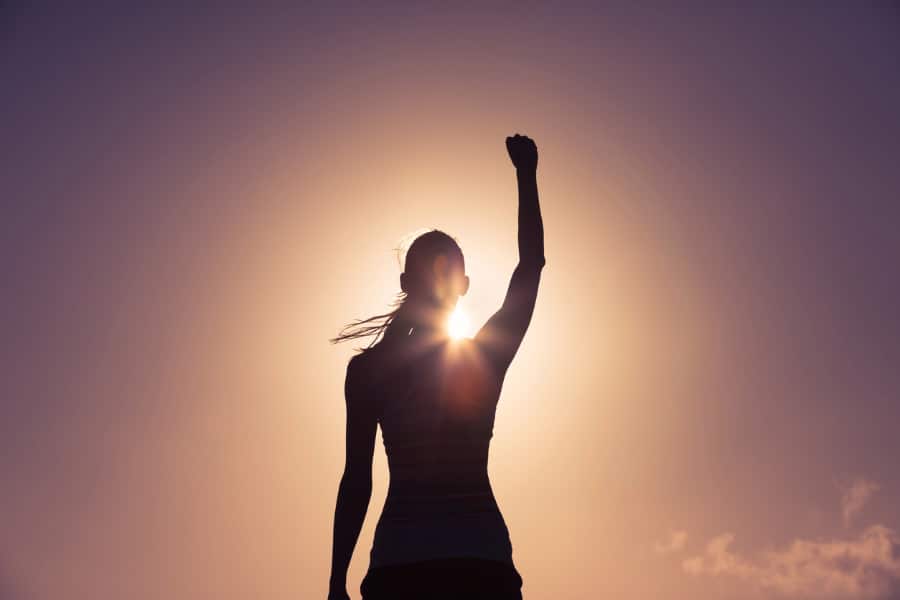 Silhouette of a woman pumping her fist in the air with the sun behind her