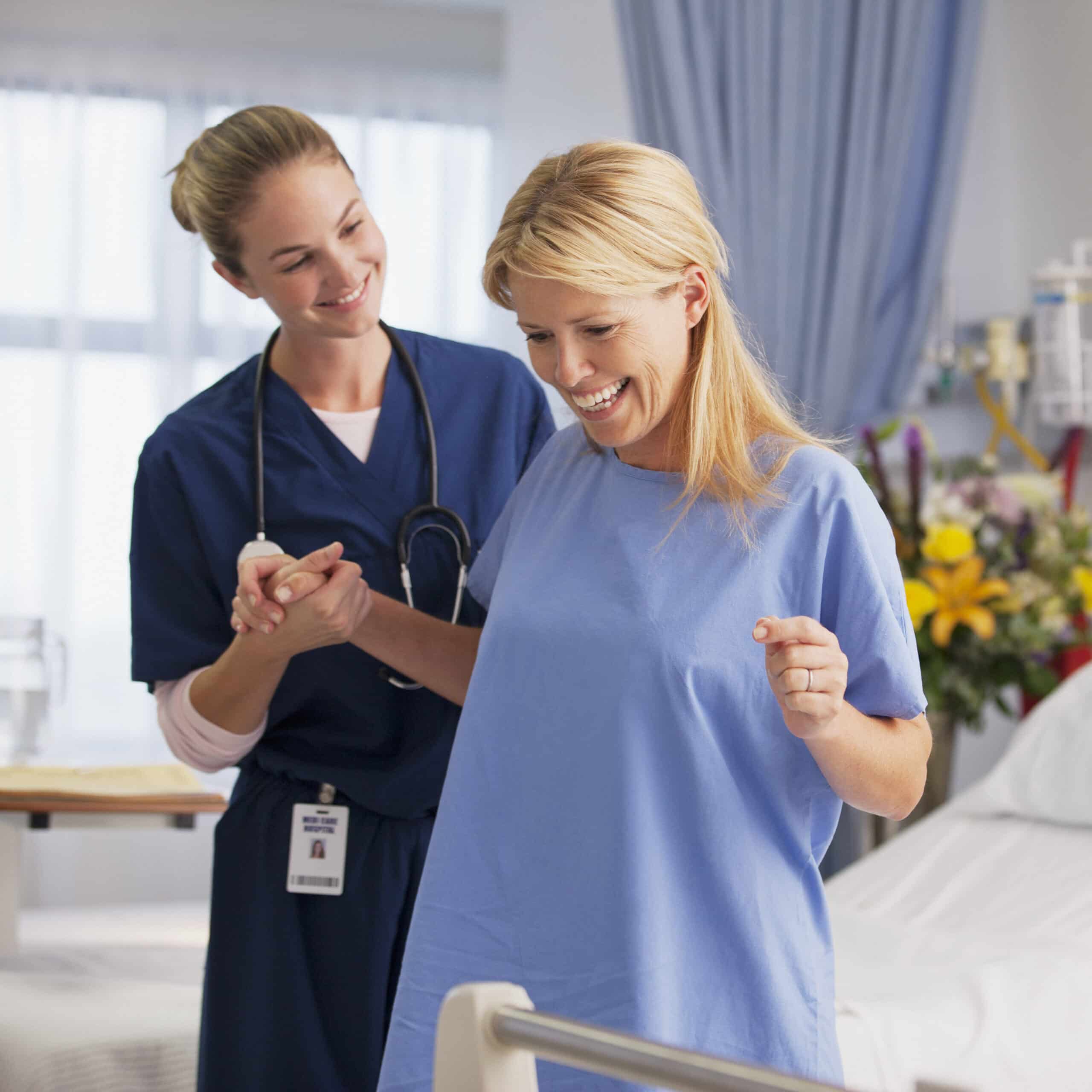 nurse helping happy patient stand in hospital room