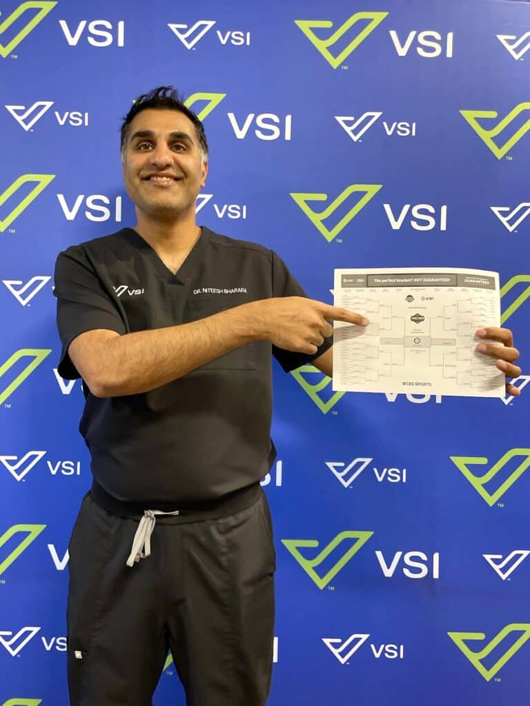 Man in black scrubs holding up March Madness bracket