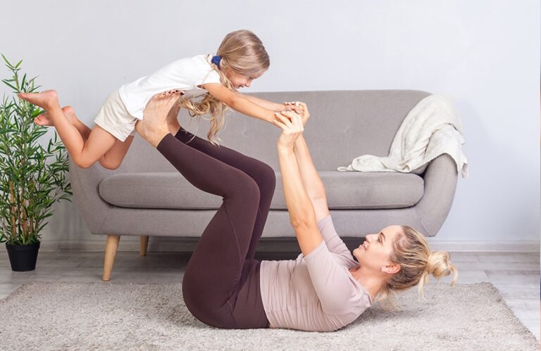 woman laying on a mat and lifting her child on her legs