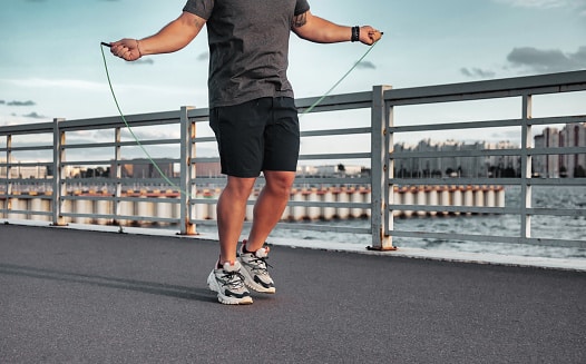 close up sportsman jumping on skipping rope in urban embankment outdoors at city background. athletic man working out with jumping rope in city district. healthy lifestyle concept. copy text space