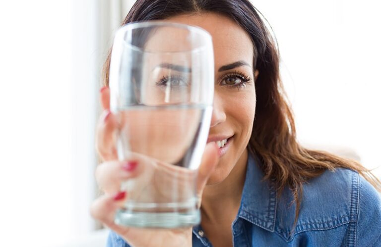 Woman holding glass of water covering half her face
