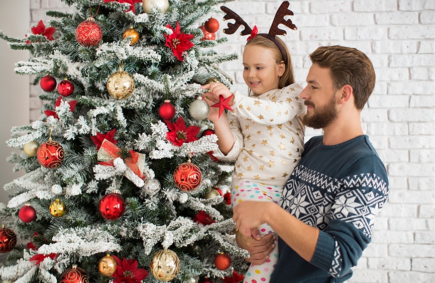 Father holding daughter and decorating a tree together
