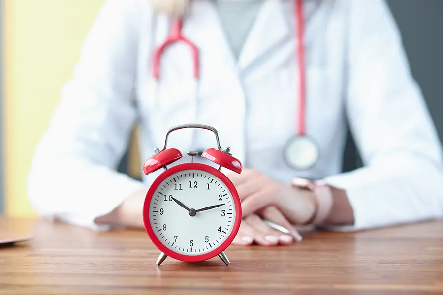 red alarm clock on background of doctor in white coat