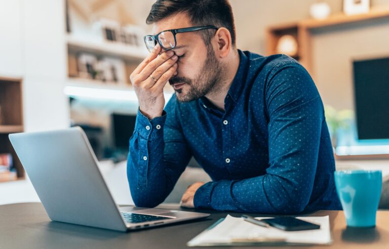 Male rubbing his eyes in front of his laptop in exhaustion