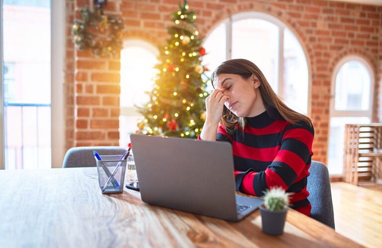 Woman stressed holding the bridge of her nose with a Christmas tree in the background